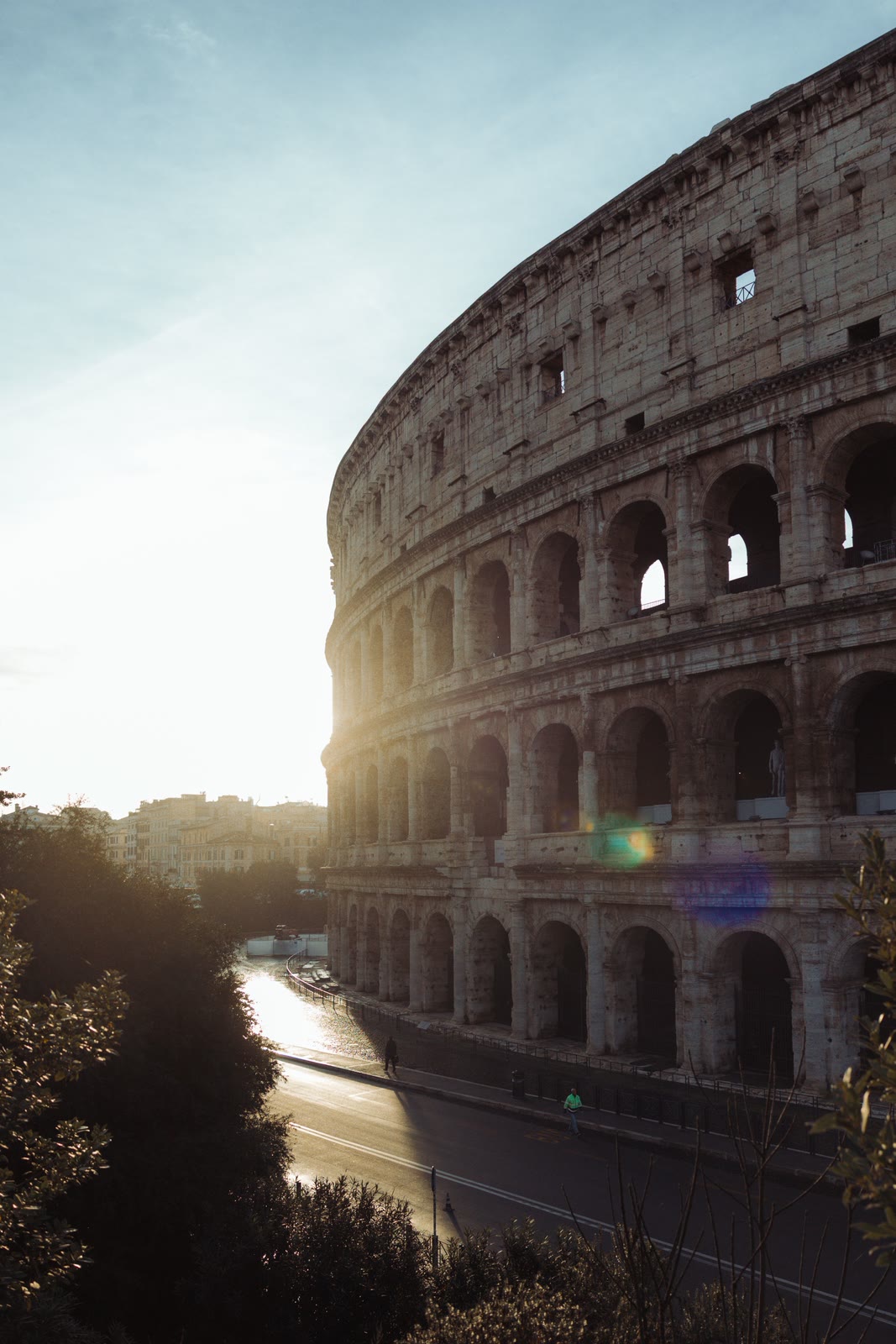 O Coliseu de Roma em contraluz ao nascer do sol, com a estrada em volta ainda vazia.