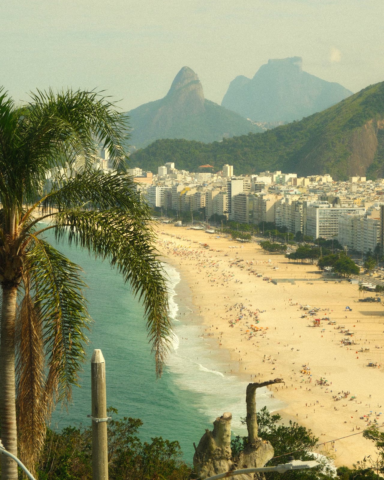 A praia de Copacabana vista de um miradouro, com o Morro Dois Irmãos e a Pedra da Gávea a fechar a baía.